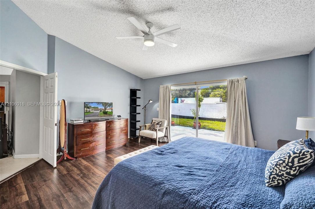 Vaulted ceiling with a central multi-blade ceiling fan, wood-finish flooring, and sliding glass doors providing outdoor access