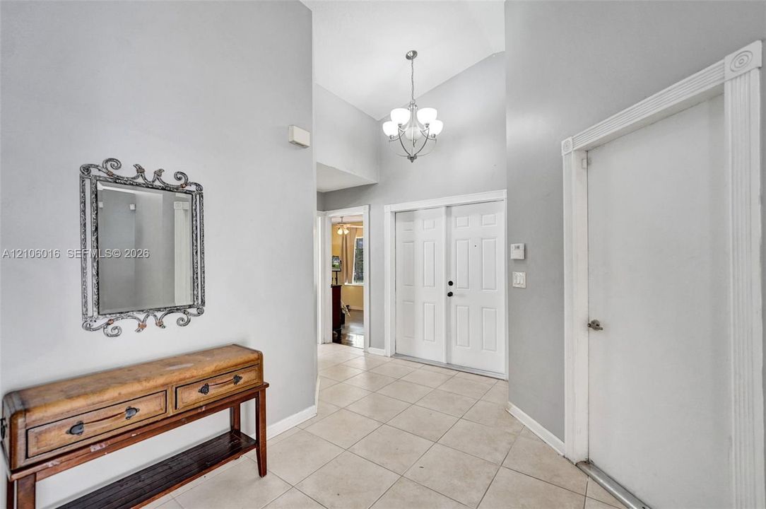 Foyer featuring vaulted ceilings, neutral ceramic tile flooring, double-door entry, and a multi-light chandelier