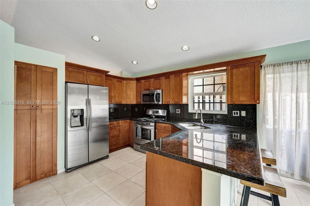 Kitchen featuring wood cabinetry, stone countertops, stainless steel appliances, tiled flooring, and recessed lighting