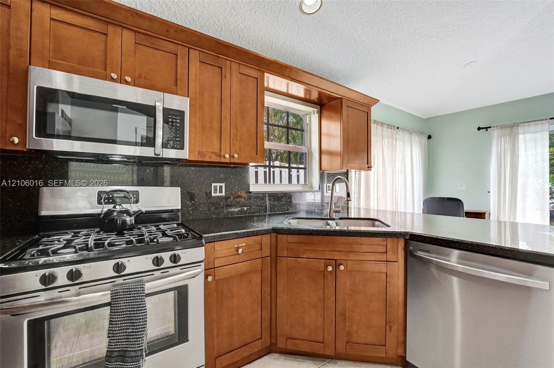 Kitchen featuring wood cabinetry, stone countertops, stainless steel gas range, over-the-range microwave, and stainless steel dishwasher
