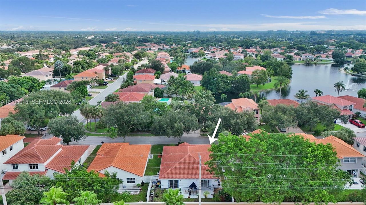 Aerial perspective of a single-story residence featuring a terracotta tile roof and mature tree canopy situated within a neighborhood setting