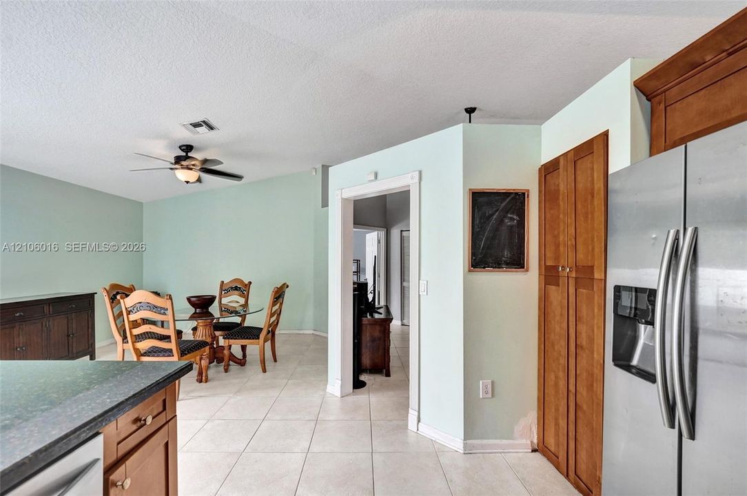Kitchen and dining area featuring wood cabinetry, tile flooring, a stainless steel refrigerator, and a ceiling fan with light fixture