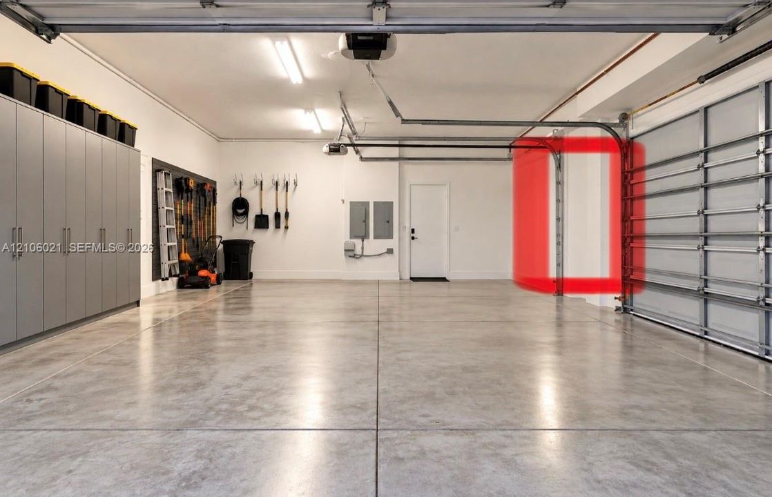 Spacious multi-car garage featuring finished concrete flooring, extensive built-in cabinetry, and LED strip lighting