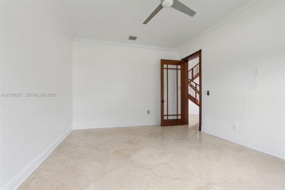 Neutral-toned stone tile flooring, crown molding, multi-pane glass-inset wooden door, and a ceiling-mounted fan