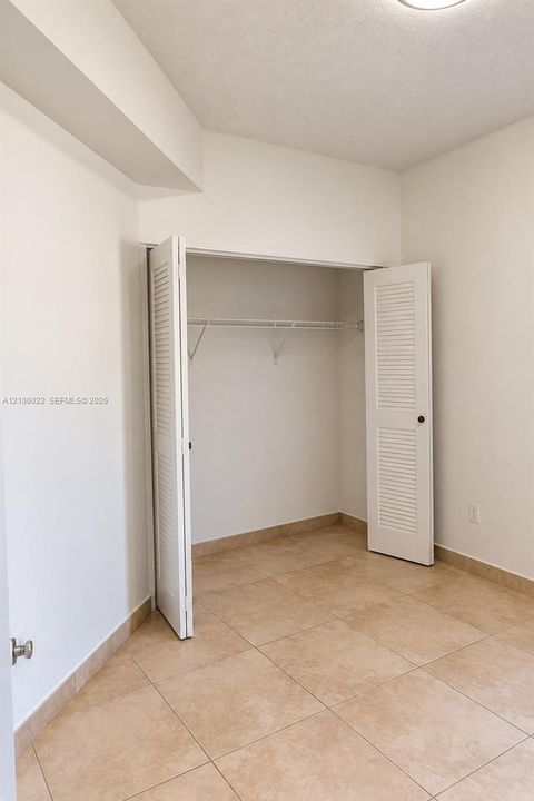 Neutral-toned ceramic tile flooring, walk-in closet with louvered bifold doors, and built-in wire shelving