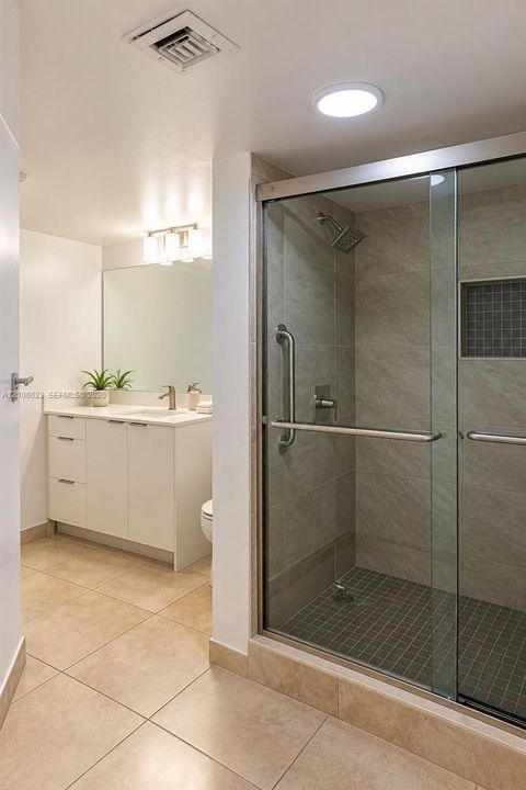 Bathroom featuring a white cabinetry vanity with integrated sink, shower enclosure with glass sliding doors, stone-finish tile surround, built-in shower niche, and large-format floor tiling