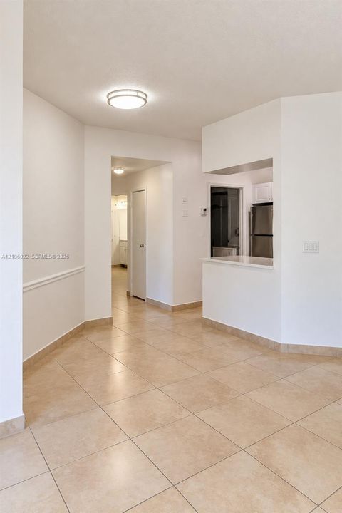 Interior space featuring large-format ceramic floor tiling, white walls, wainscoting detail, ceiling-mounted light fixtures, and a pass-through counter