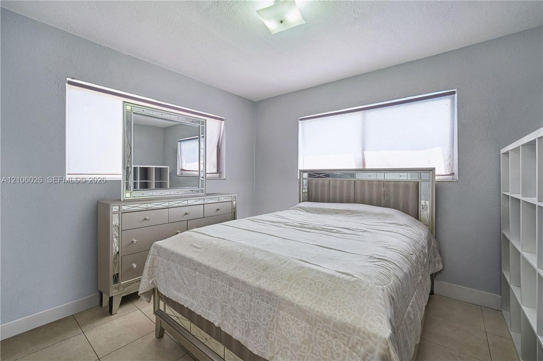 Neutral-toned walls, large windows with fitted roller shades, square ceramic tile flooring, and a ceiling-mounted light fixture