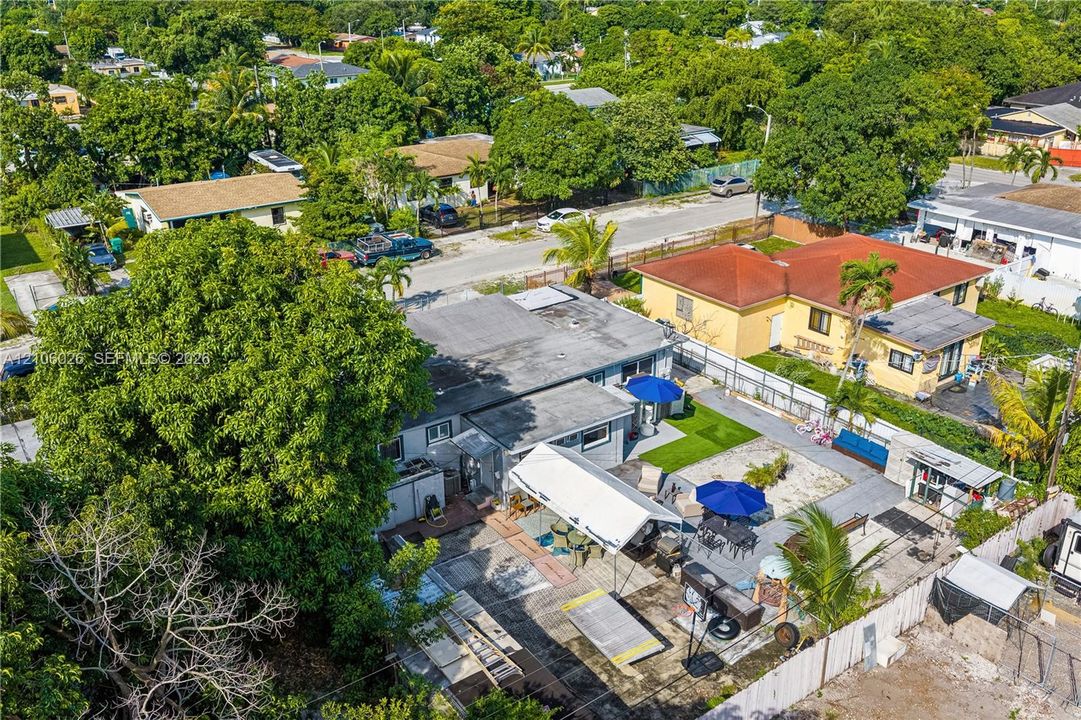 Aerial perspective of a property featuring a paved outdoor patio, structural canopy, fenced perimeter, and mature trees within a residential setting