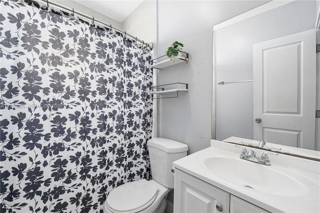 Bathroom featuring a white vanity cabinet with an integrated oval basin, chrome-finished dual-handle faucet, large wall-mounted mirror, and tiered white wall shelving