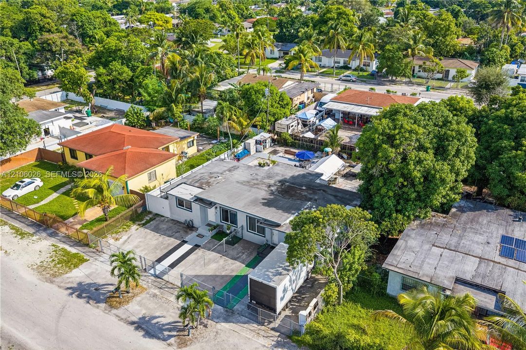 Aerial perspective of a single-story residence featuring a flat roof, concrete exterior finish, paved driveway, and perimeter fencing