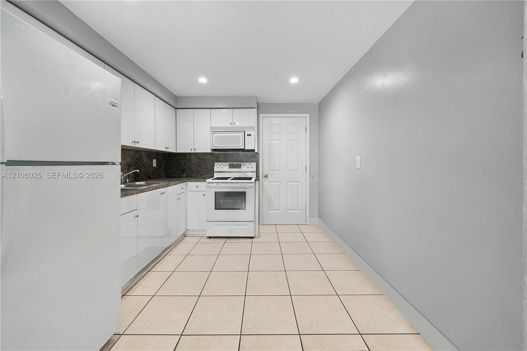 Kitchen featuring white slab-front cabinetry, stone-finish countertops, tile flooring, recessed lighting, and white appliances