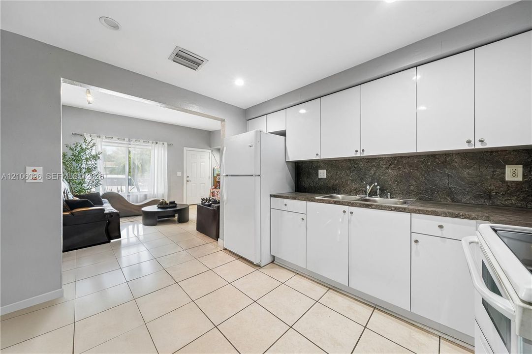 Kitchen featuring white flat-panel cabinetry, dark stone-finish countertops, tile flooring, and recessed lighting