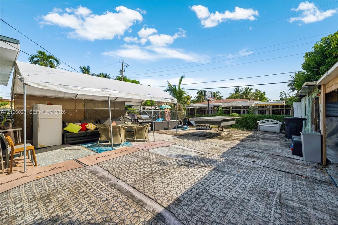 Expansive paved patio area featuring a fixed fabric-covered canopy, perimeter fencing, and mature palm trees