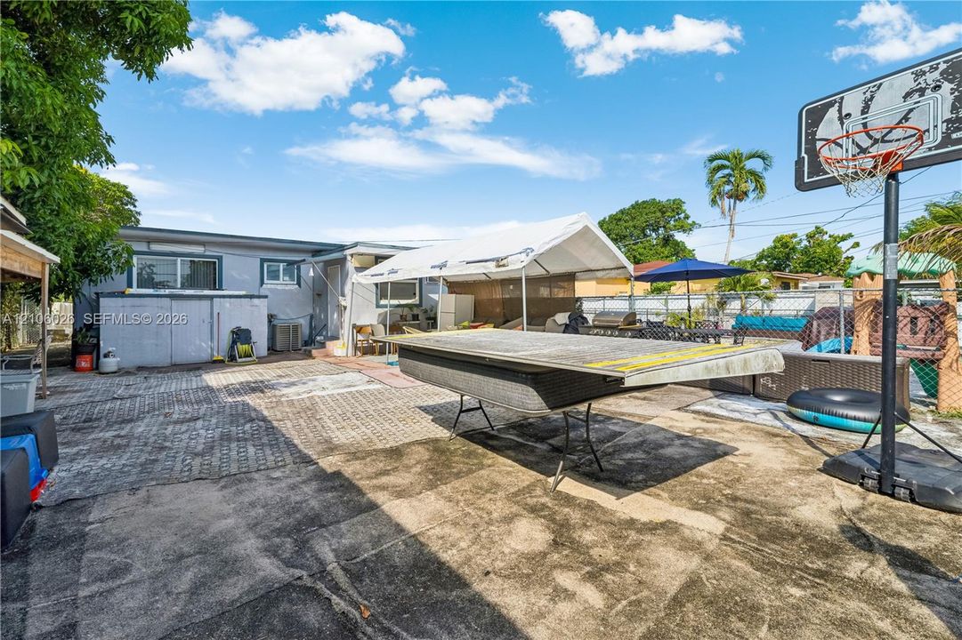 Extensive concrete patio area featuring a metal-framed structure, chain-link perimeter fencing, and mature palm trees