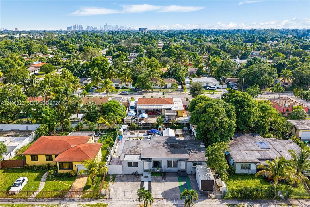 Aerial perspective of a suburban neighborhood featuring low-density residential lots, mature tree canopy, and a distant cityscape skyline