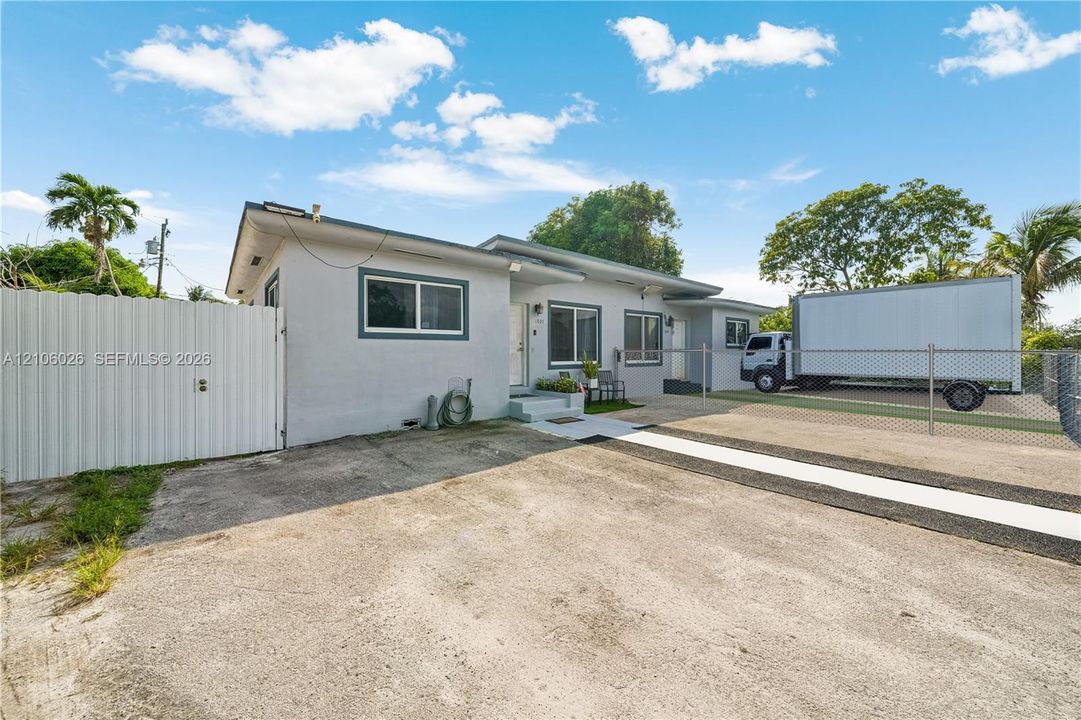 Single-story exterior featuring a concrete facade, white panel privacy fencing, and a paved driveway