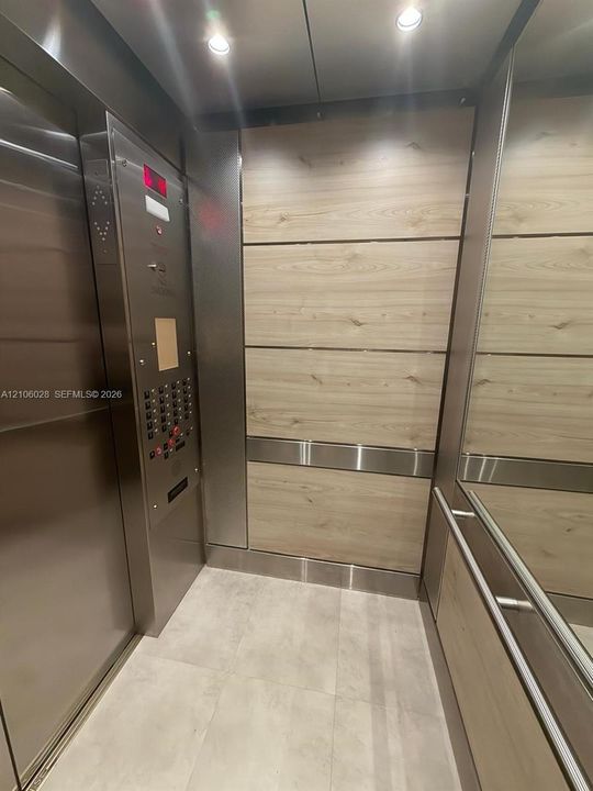 Elevator cab featuring wood-finish paneling, stainless steel trim, integrated mirror, brushed metal control panel, and recessed ceiling lighting