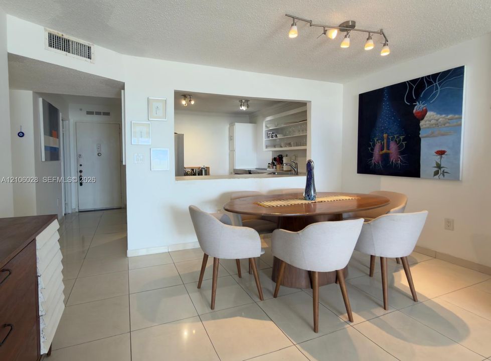 Dining area featuring large-format ceramic tile flooring, a pass-through window to the kitchen, and a six-light track fixture