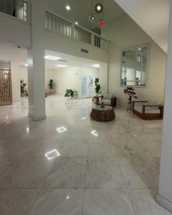 Expansive foyer featuring polished stone flooring, vaulted ceilings, a structural support column, and a railed upper-level balcony
