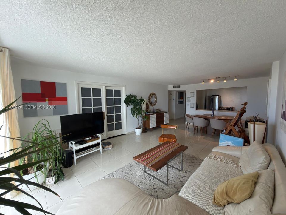 Living area featuring large-format tile flooring, multi-pane glass sliding doors, and an open pass-through window to the kitchen area