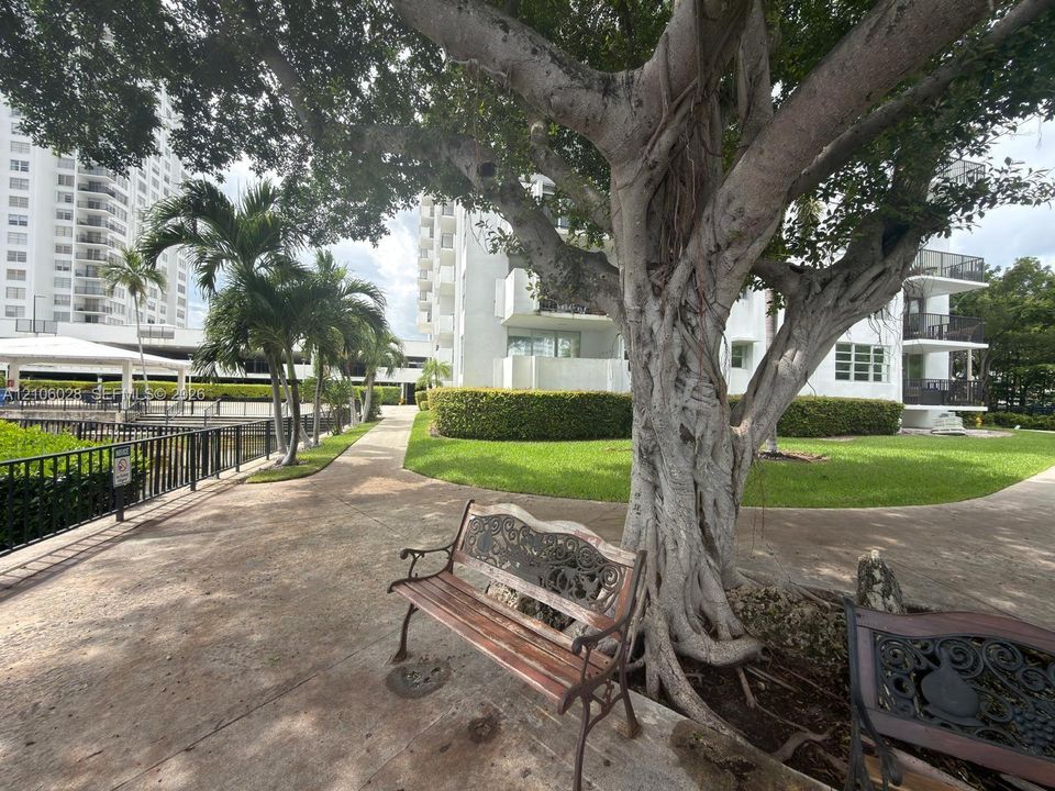 Landscaped grounds featuring mature trees, manicured hedges, paved walking paths, and metal perimeter fencing