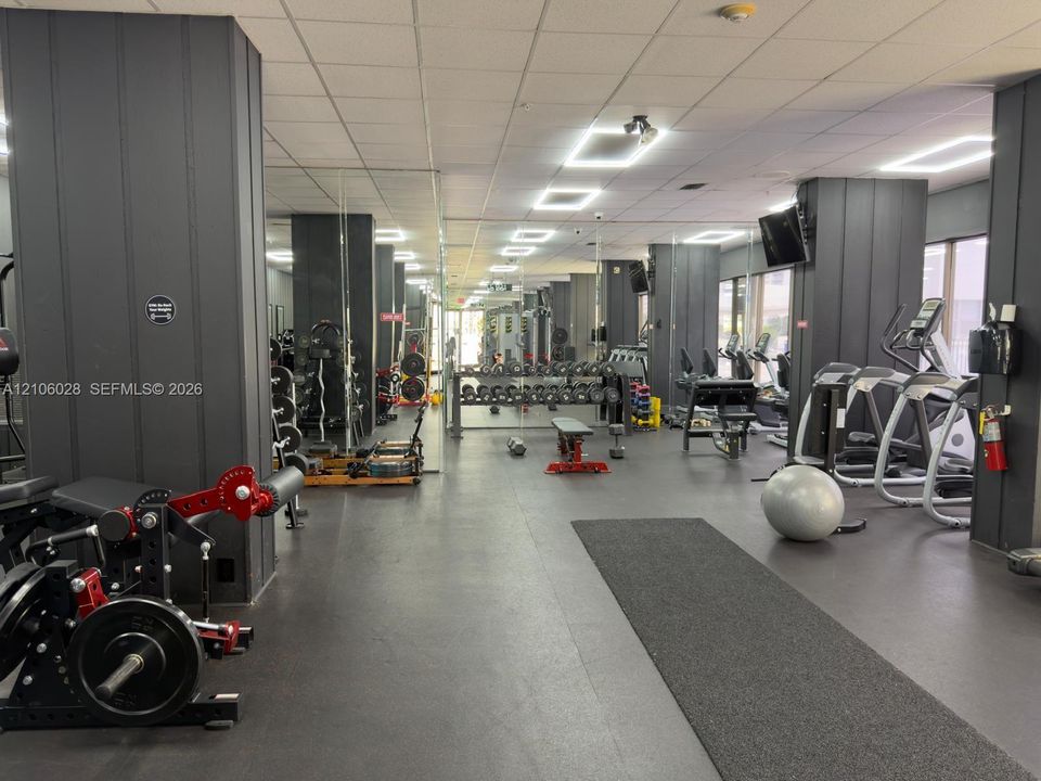 Fitness facility featuring full-wall mirrors, recessed ceiling lighting, dark-toned vertical wall paneling, and rubberized flooring