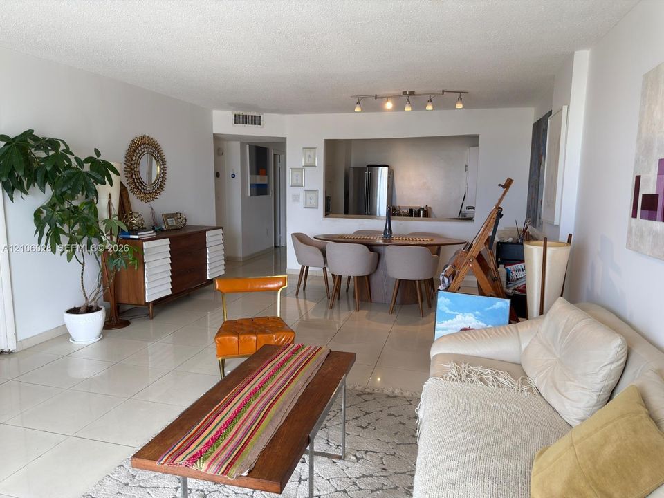 Open-concept area featuring light-toned tile flooring, neutral wall finishes, a multi-head track lighting fixture, and a pass-through kitchen opening