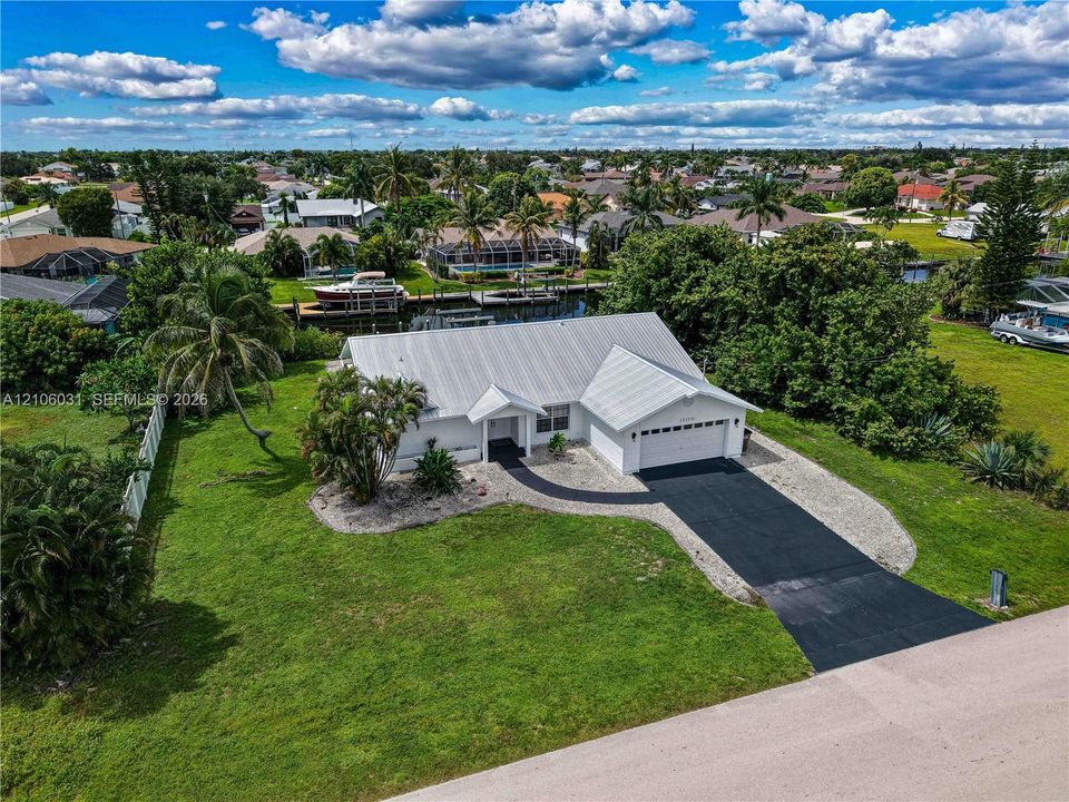 Waterfront property featuring a metal roof, attached two-car garage, paved driveway, and expansive lawn area