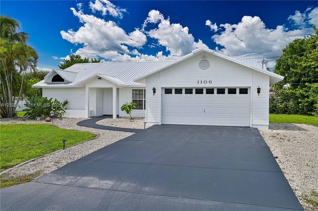White exterior residence featuring a standing seam metal roof, attached two-car garage with glass-paneled door, and paved driveway