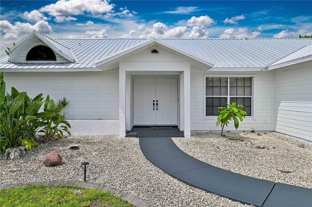 Exterior facade featuring white horizontal siding, a metal roof, a semi-circular accent window, and double entry doors