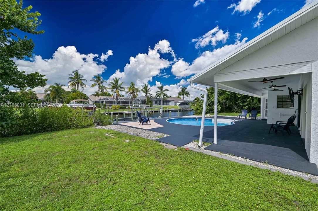 Covered patio featuring two ceiling fans, in-ground swimming pool, concrete pool deck, and private boat dock situated on a canal