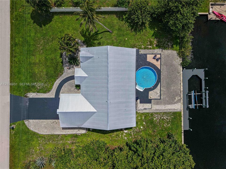 Waterfront property featuring a metal roof, a private boat dock with lift, an inground circular pool, and paved driveway