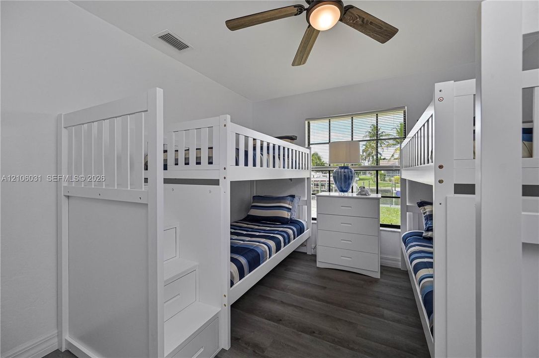 Room featuring wood-finish flooring, a multi-blade ceiling fan with integrated lighting, and a window with exterior water and landscape surroundings