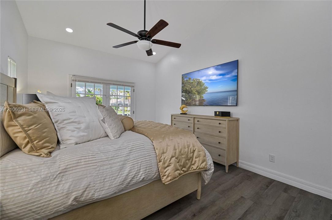 Vaulted ceiling with integrated recessed lighting, wood-finish flooring, and a multi-blade ceiling fan