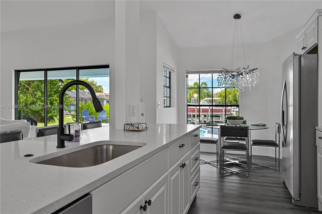 Kitchen featuring a quartz countertop, stainless steel undermount sink, matte black gooseneck faucet, white shaker-style cabinetry, and wood-finish flooring