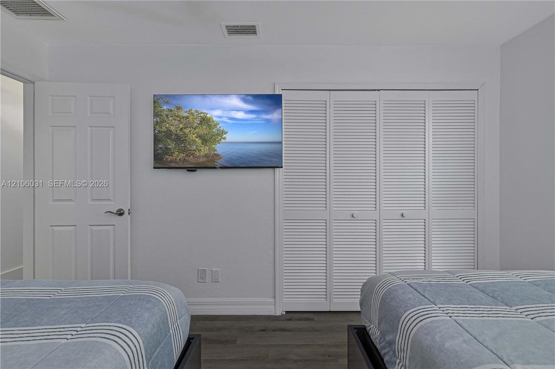 Room featuring wood-finish flooring, white louvered-style closet doors, and a solid-panel interior door with a brushed nickel lever handle