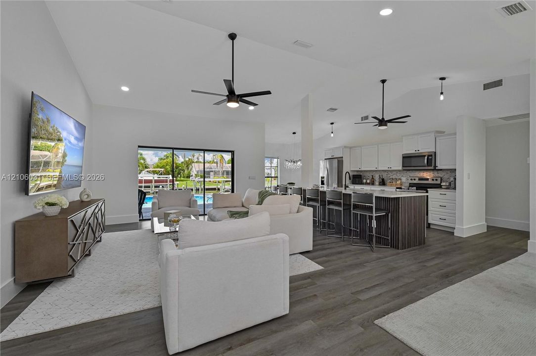 Open-concept interior featuring vaulted ceilings, wood-finish flooring, a kitchen island with cabinetry seating, and large sliding glass doors