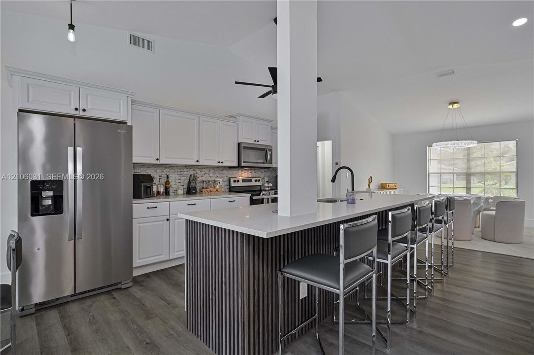 Kitchen featuring white cabinetry, wood-finish flooring, a central island with a slatted wood base and quartz countertop, stainless steel appliances, and a mosaic tile backsplash
