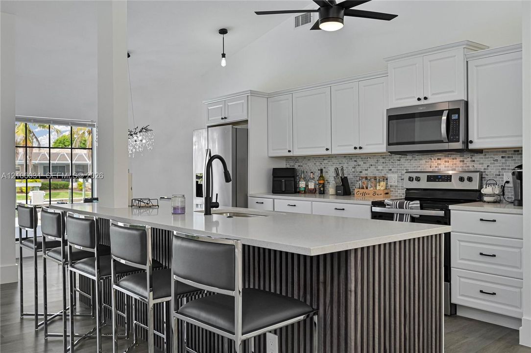 Kitchen featuring white shaker-style cabinetry, quartz countertops, a slatted wood-finish kitchen island, a mosaic tile backsplash, and stainless steel appliances