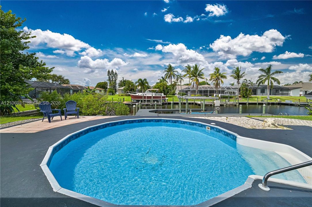 In-ground pool with integrated steps, canal frontage, private boat dock, and paved poolside patio