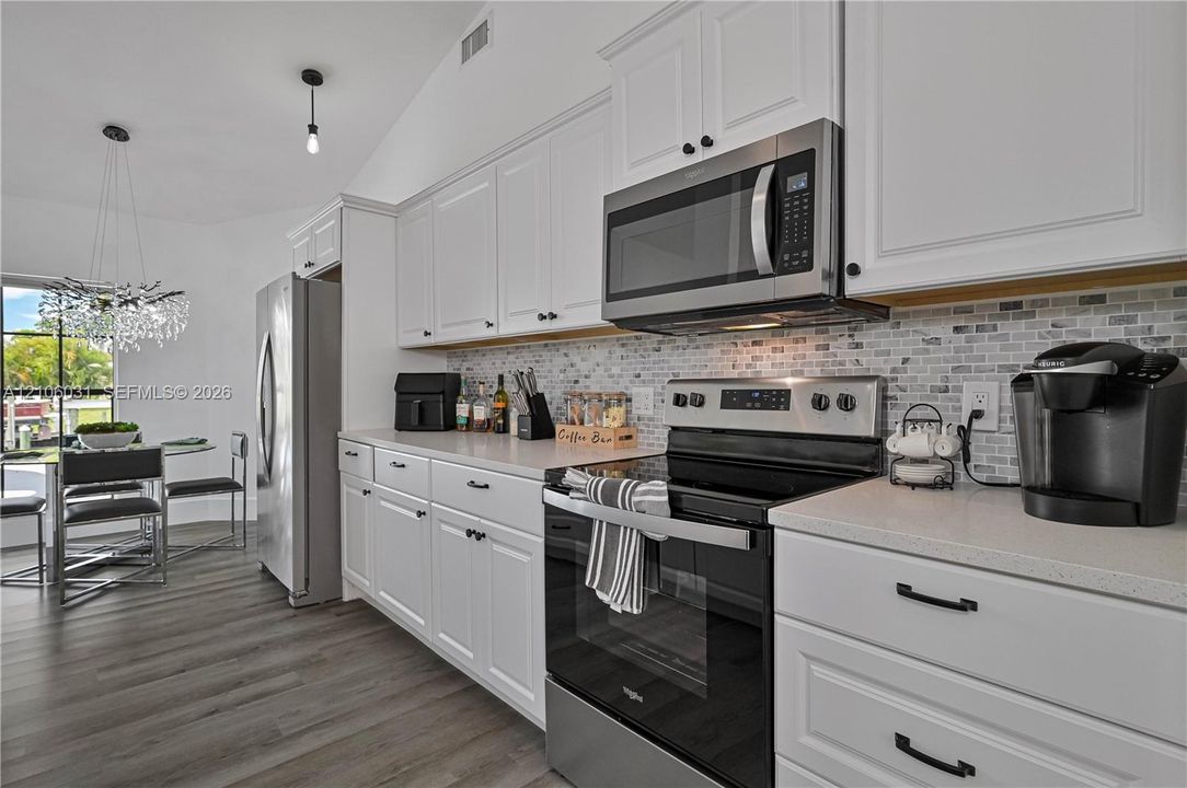 Kitchen featuring white Shaker-style cabinetry, stainless steel appliances, a mosaic tile backsplash, quartz countertops, and wood-finish flooring