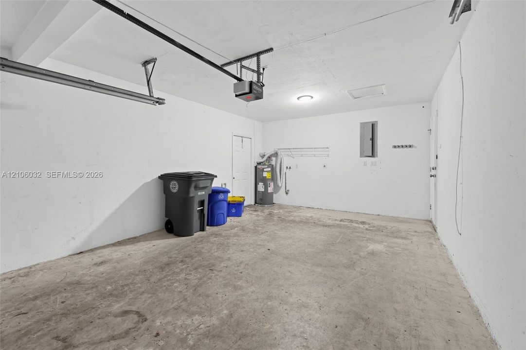 Enclosed garage space featuring a concrete floor, painted walls, ceiling-mounted garage door opener, and integrated electrical service panel