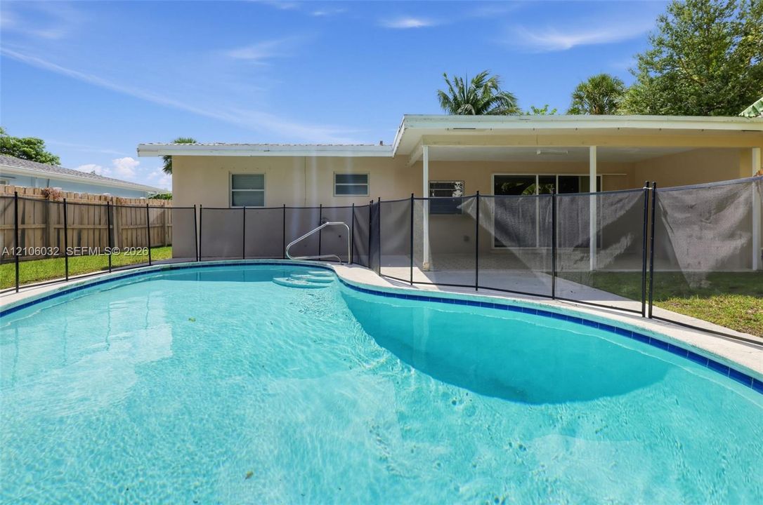 In-ground swimming pool featuring a mesh safety fence, concrete pool deck, and a covered rear patio