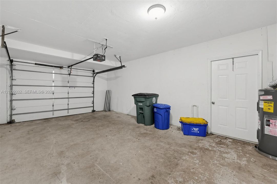 Garage featuring a concrete floor, white walls, automated overhead door, and a six-panel pedestrian door