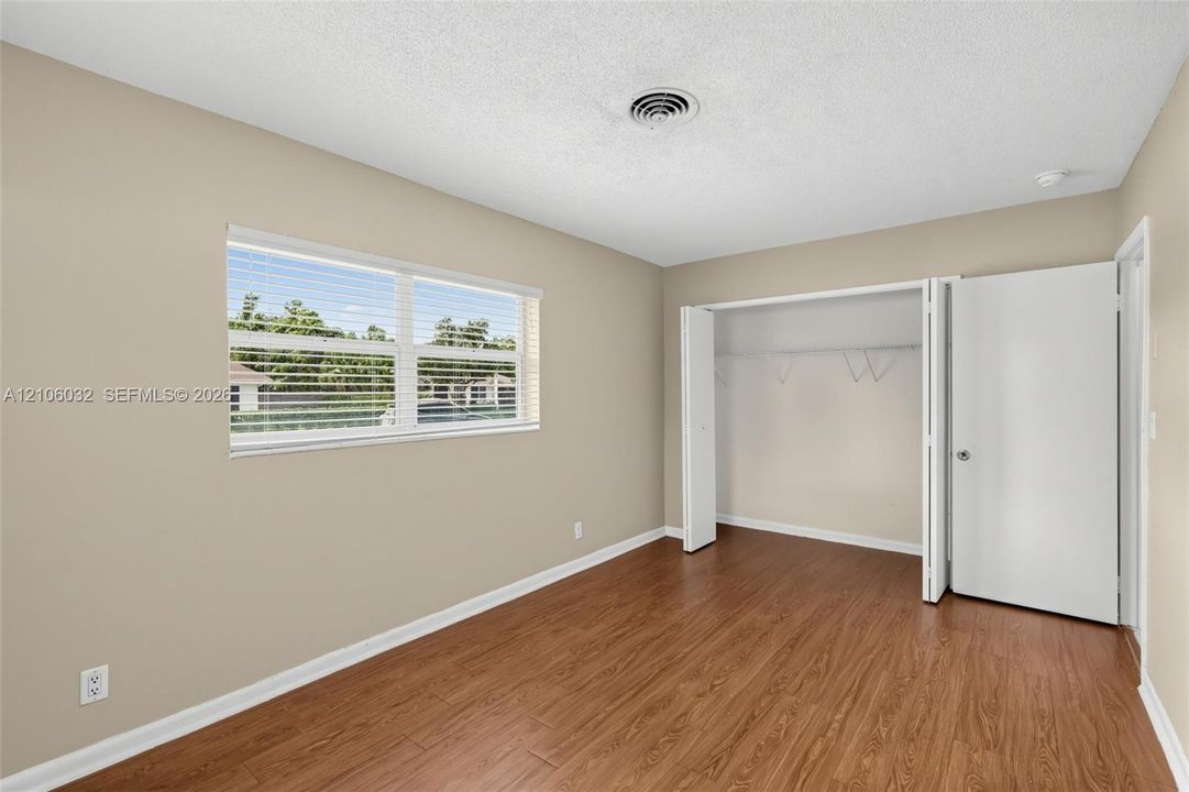Room featuring wood-finish flooring, a large window with horizontal blinds, neutral wall paint, and a built-in closet with folding doors