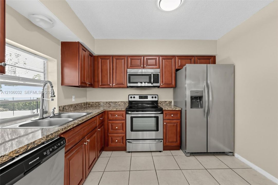 Kitchen featuring stained wood cabinetry, stone-finish countertops, stainless steel appliances, and ceramic tile flooring