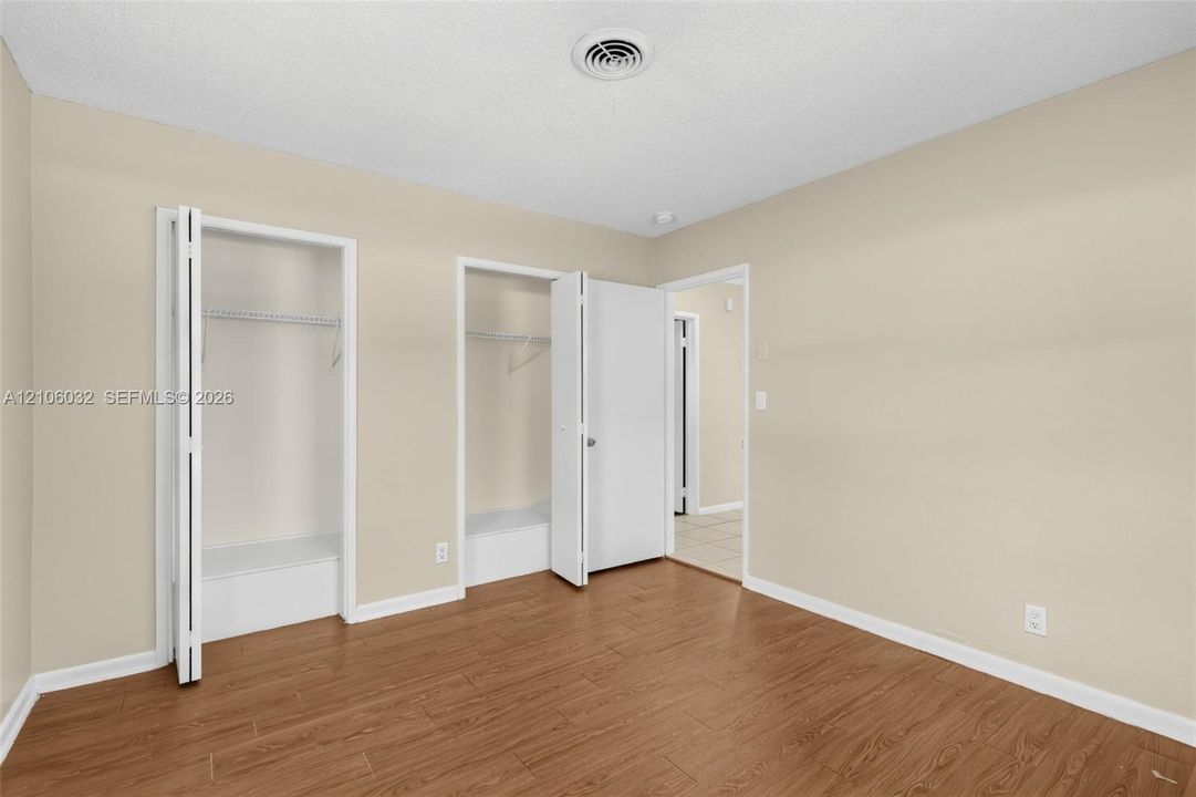 Wood-finish flooring, neutral wall tones, and dual closets featuring white doors and integrated shelving