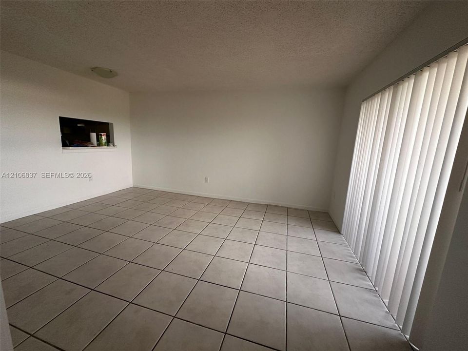 Room featuring neutral tile flooring, vertical window blinds, and a built-in wall pass-through