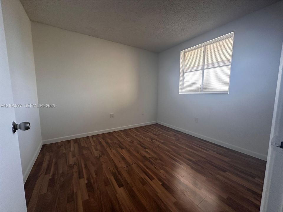 Wood-finish flooring, neutral wall tones, and single-pane window with horizontal blinds